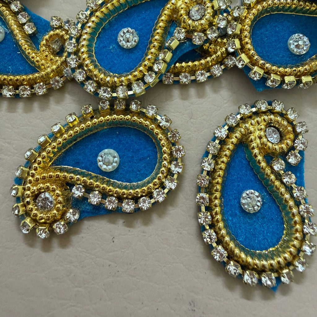 Decorative blue and gold paisley designs with crystals on a beige background