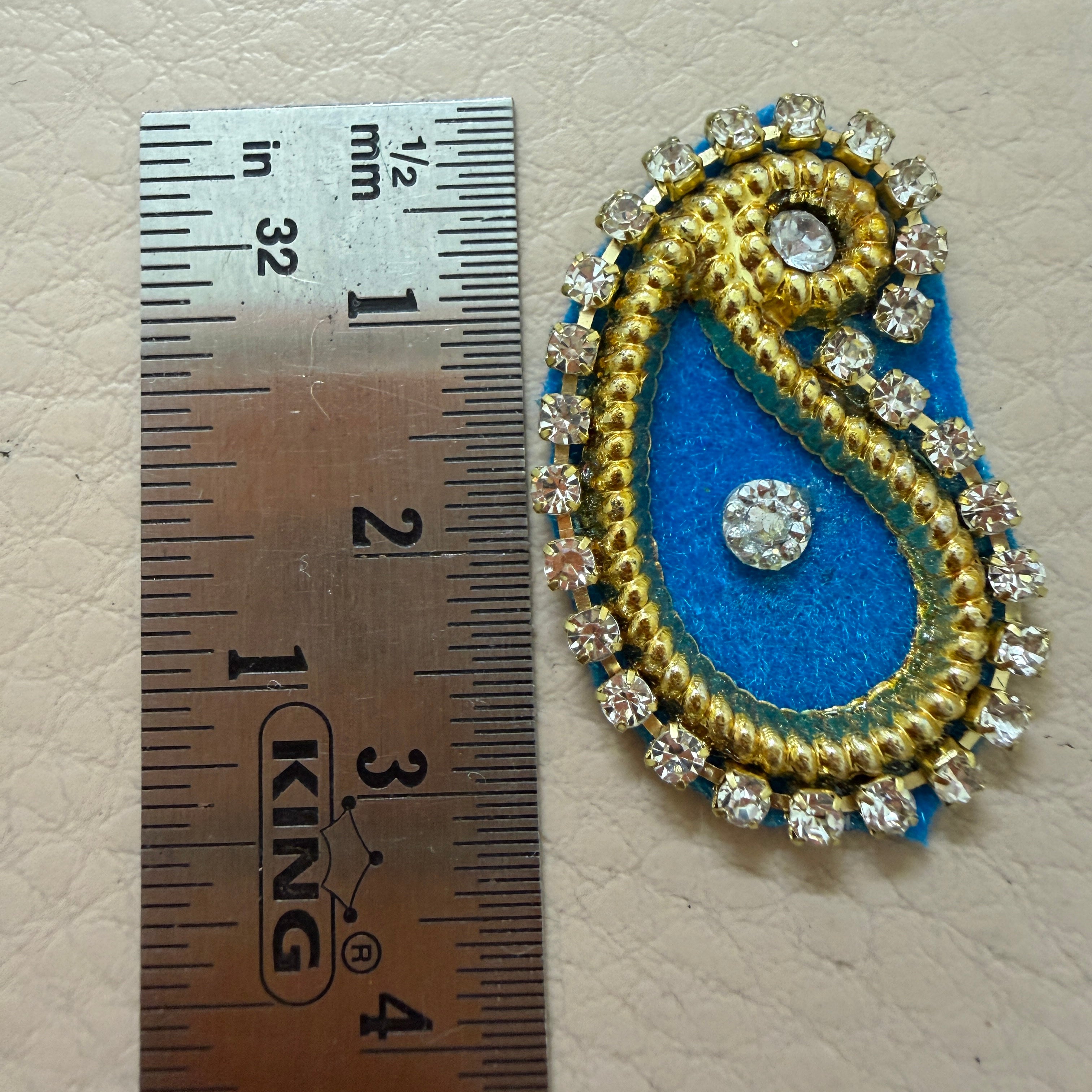 Decorative paisley patch with blue center and gold border next to a ruler for scale.