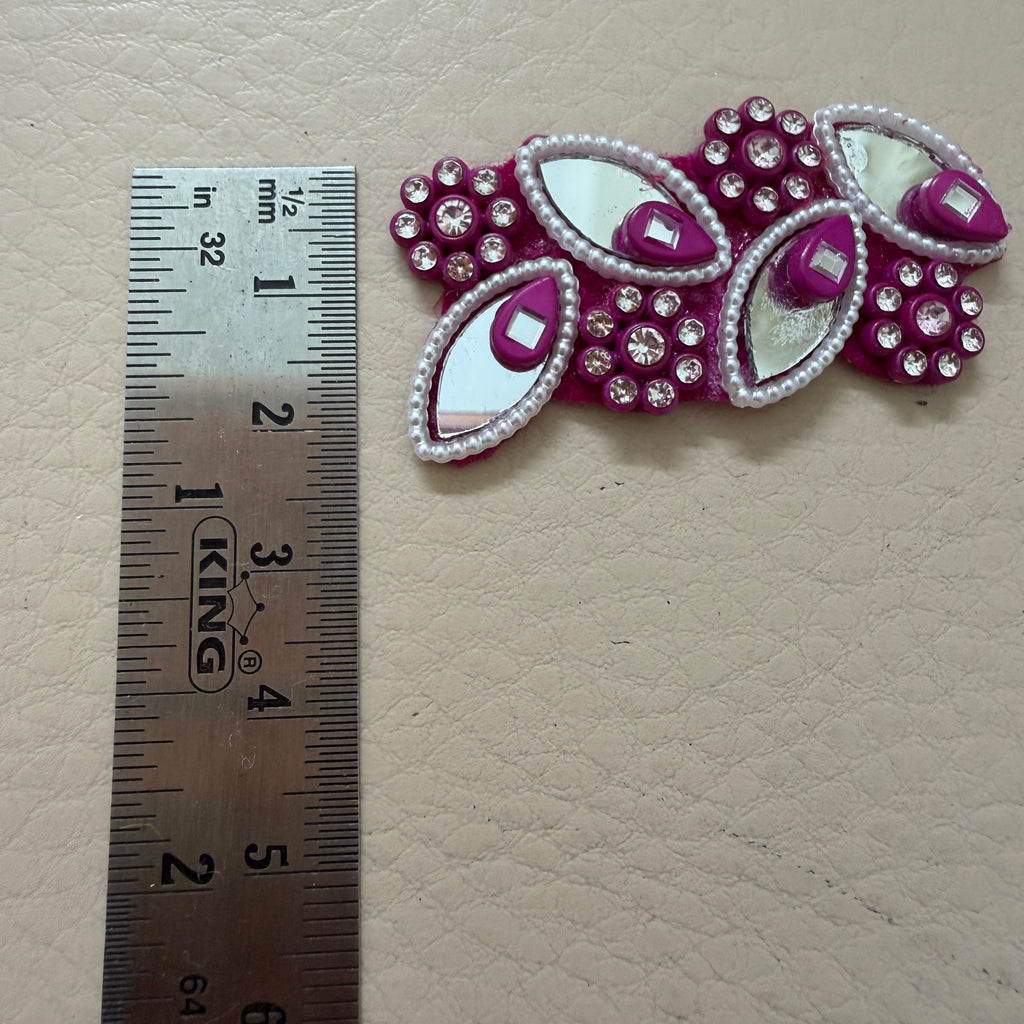 Decorative pink and silver leaf-shaped embellishment with a ruler for scale on a beige background