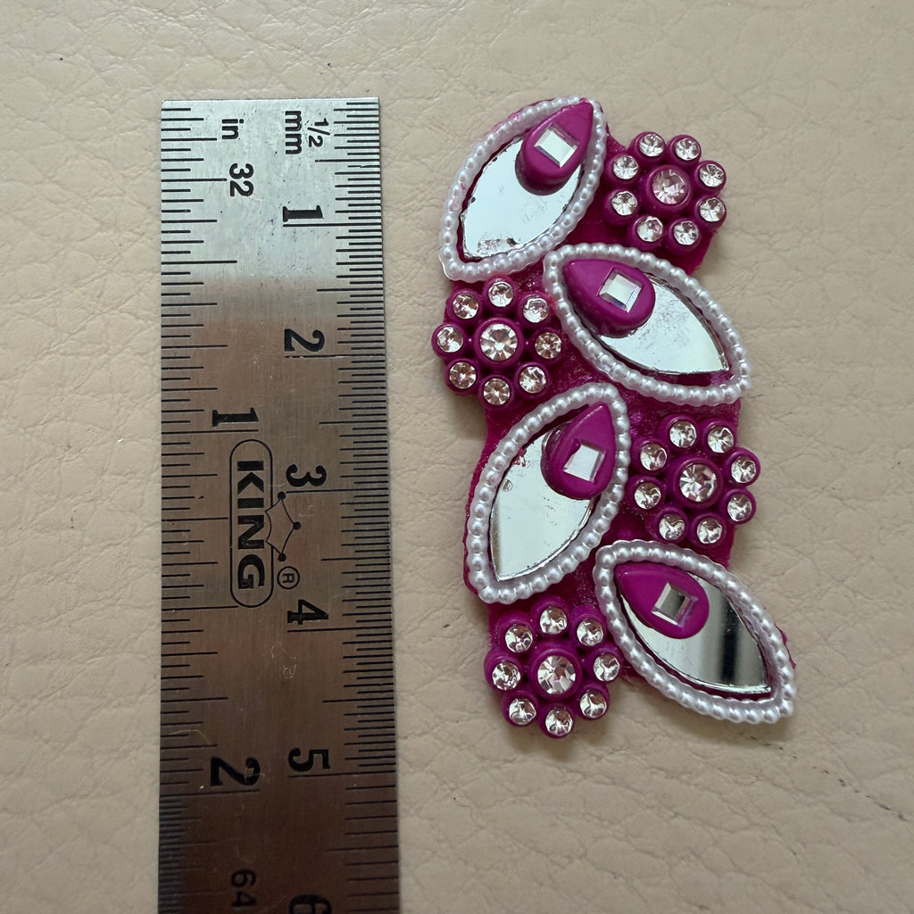 Decorative pink and silver embellishment with a ruler for scale on a beige background