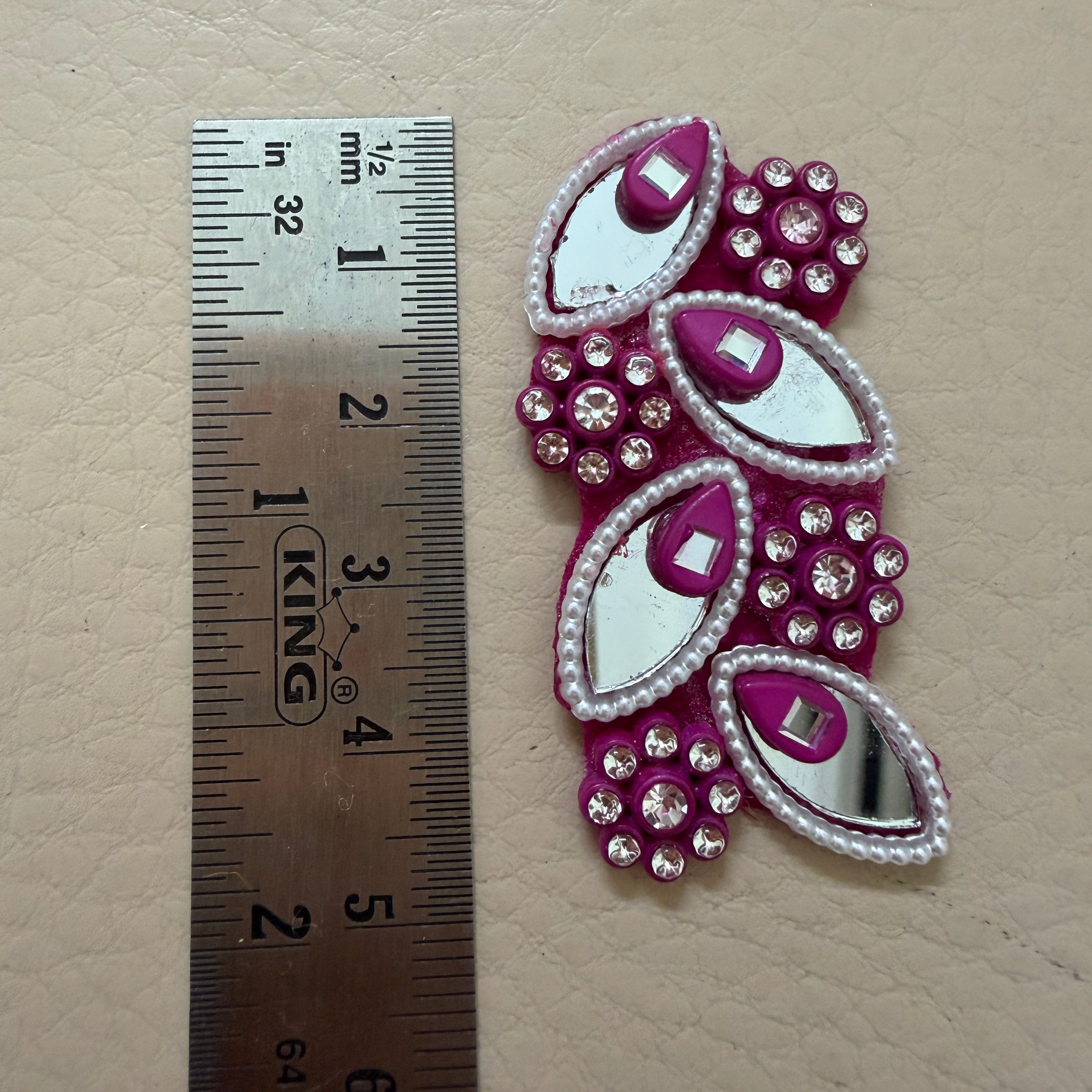 Decorative pink and silver embellishment with a ruler for scale on a beige background