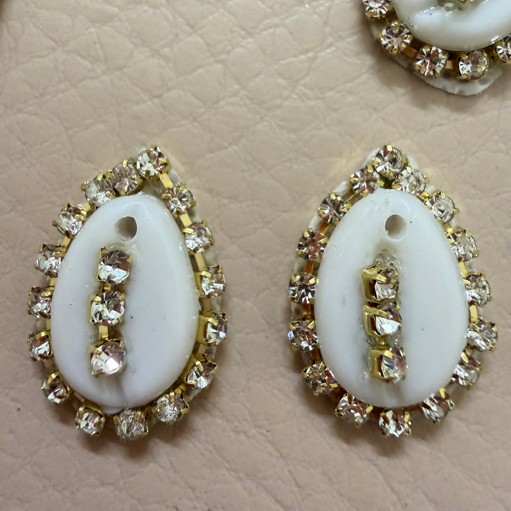 Pair of white oval stones with gold and clear gemstone accents on a beige textured background