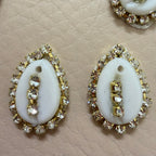Pair of white oval stones with gold and clear gemstone accents on a beige textured background