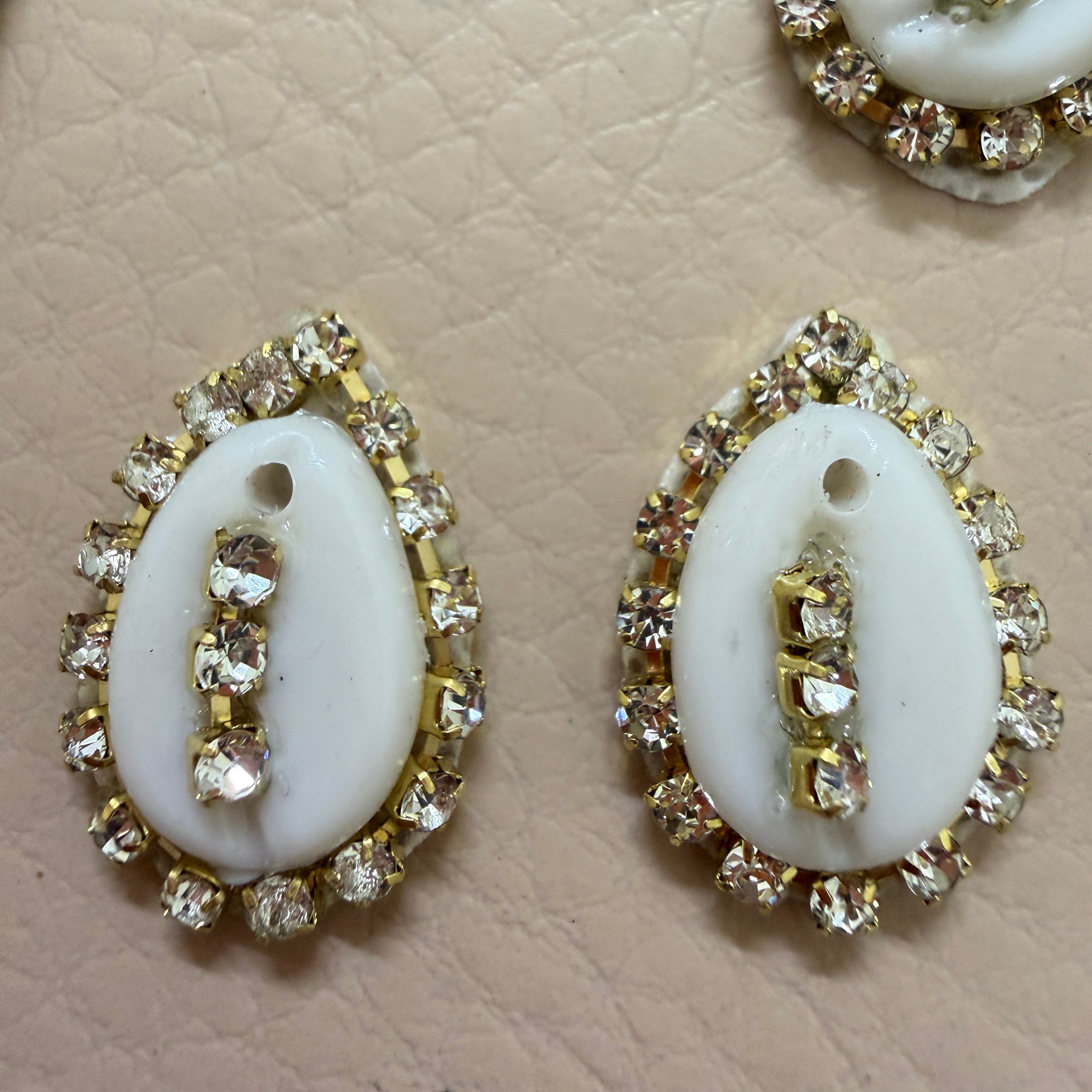 Pair of white oval stones with gold and clear gemstone accents on a beige textured background