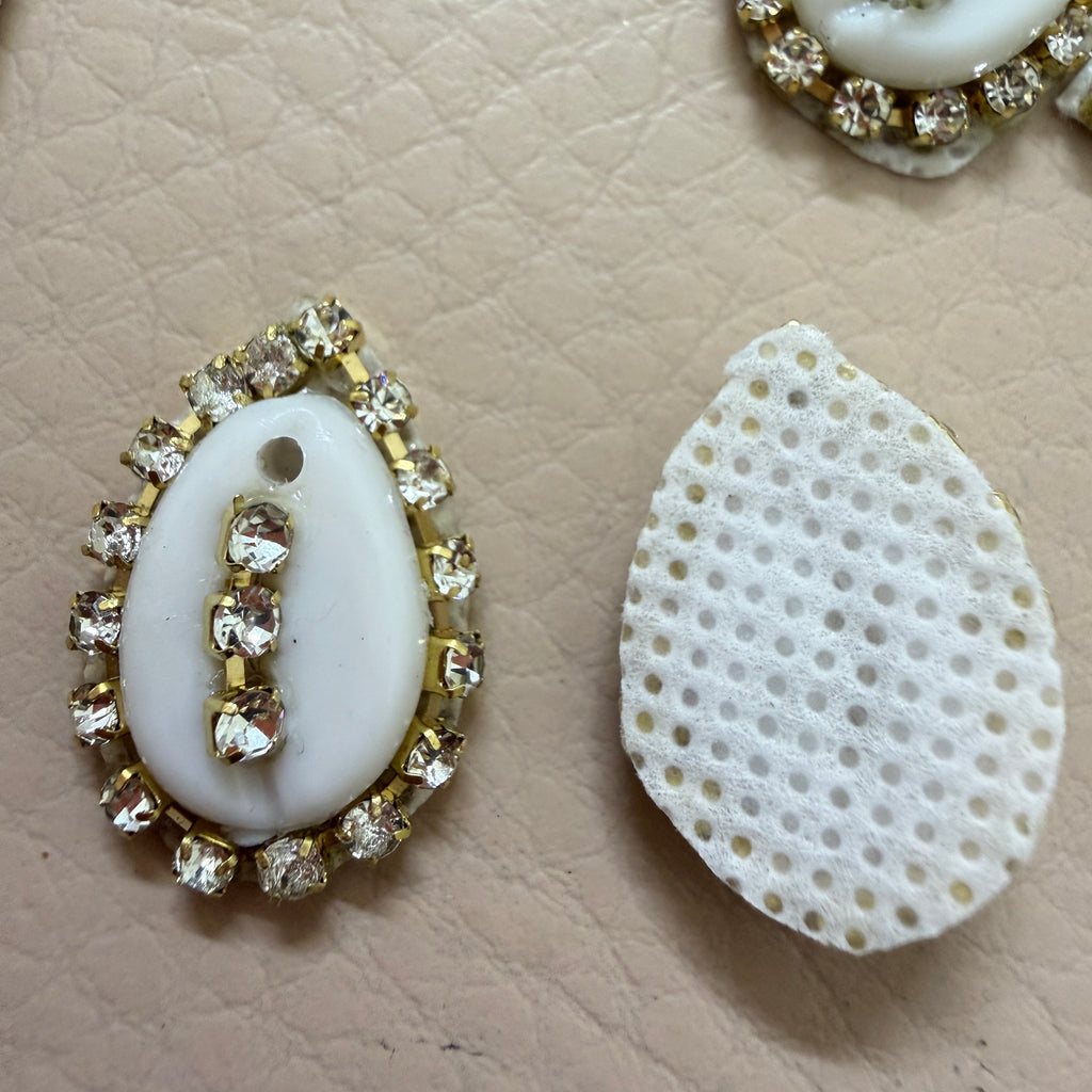 Decorative white stone with gold and crystal embellishments on a beige textured surface.