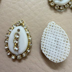 Decorative white stone with gold and crystal embellishments on a beige textured surface.