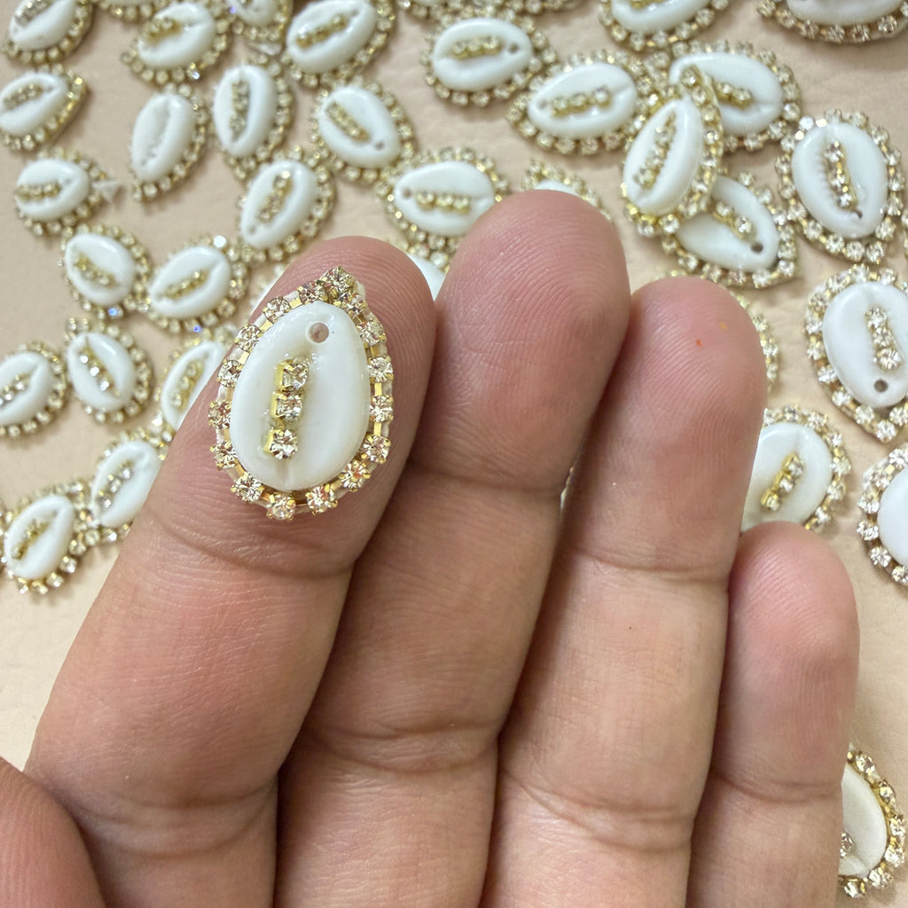 Decorative white shell with gold accents held between fingers against a patterned background