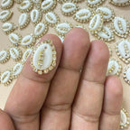 Decorative white shell with gold accents held between fingers against a patterned background