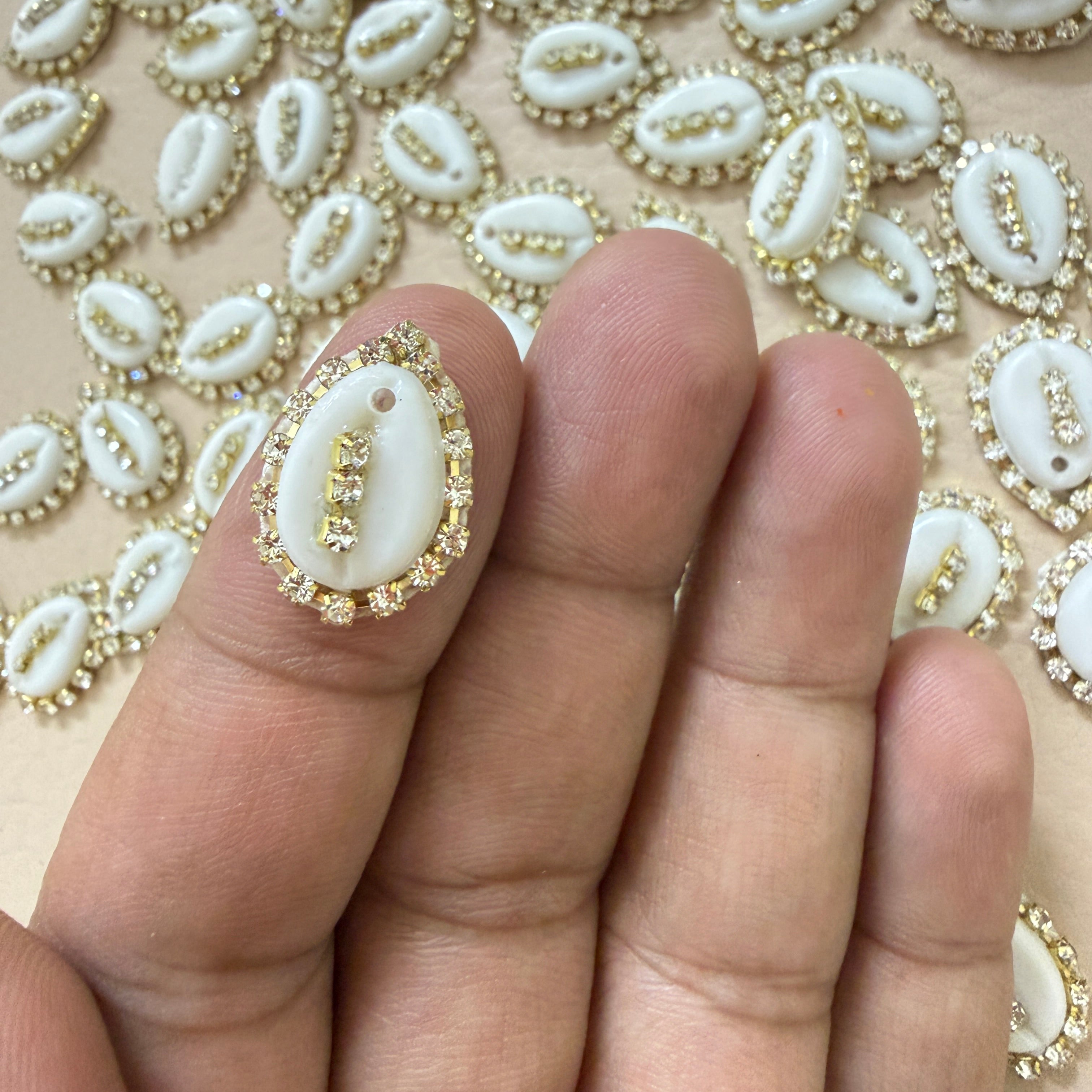 Decorative white shell with gold accents held between fingers against a patterned background