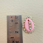 Pink oval pendant with decorative elements next to a ruler for scale on a beige background