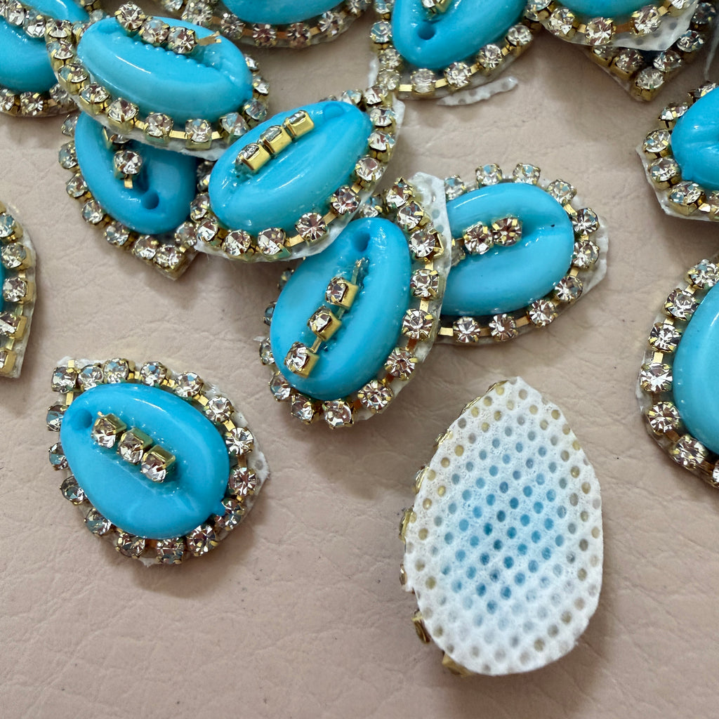Blue teardrop-shaped embellishments with rhinestones on a beige surface