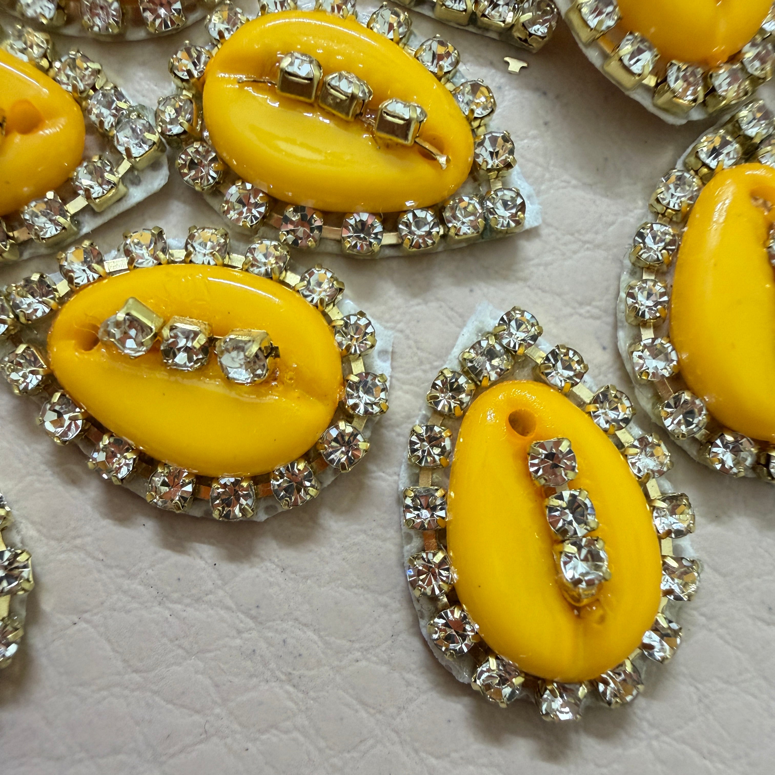 Yellow oval-shaped buttons with rhinestone embellishments on a textured surface
