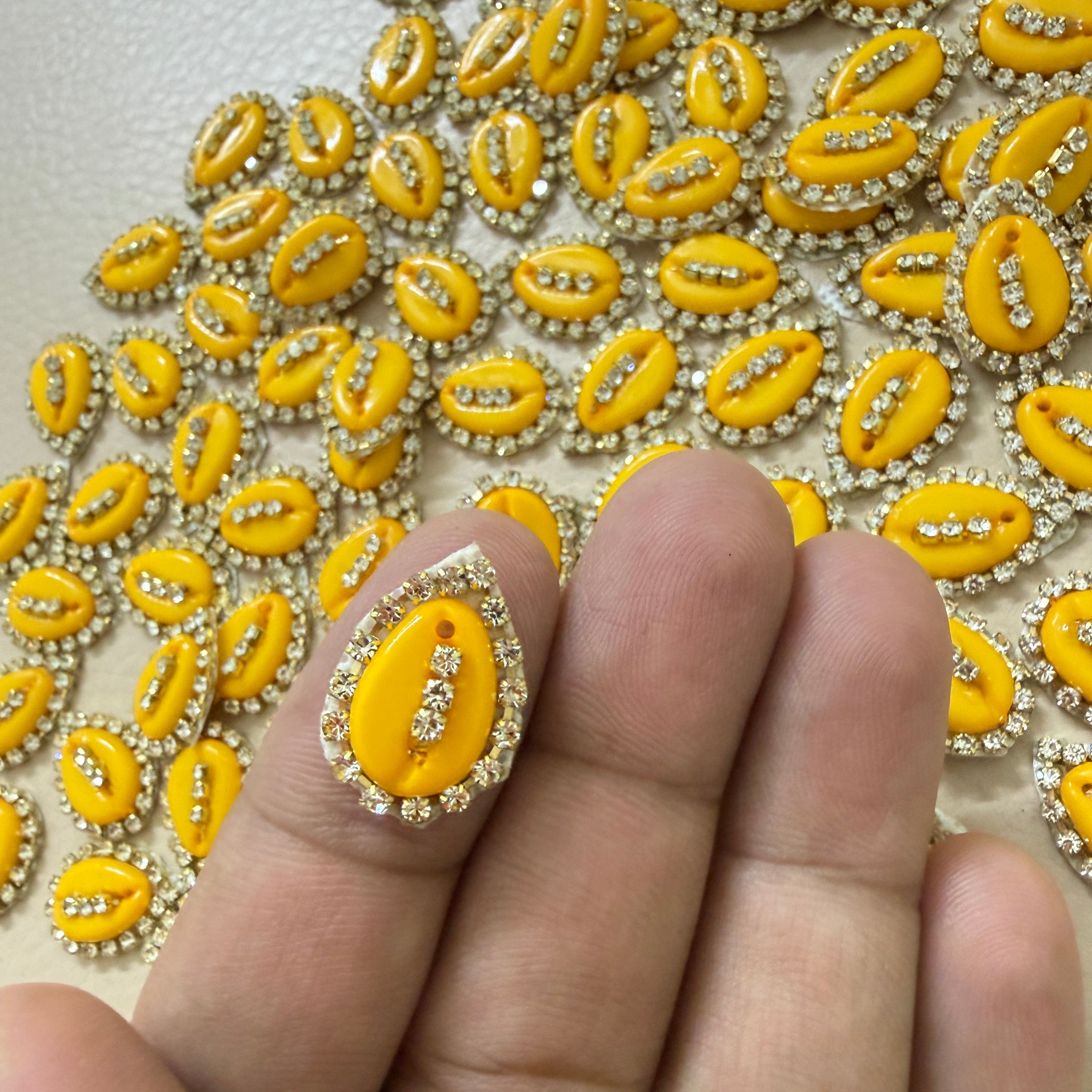 Close-up of a hand holding a yellow decorative element with rhinestones against a matching background.