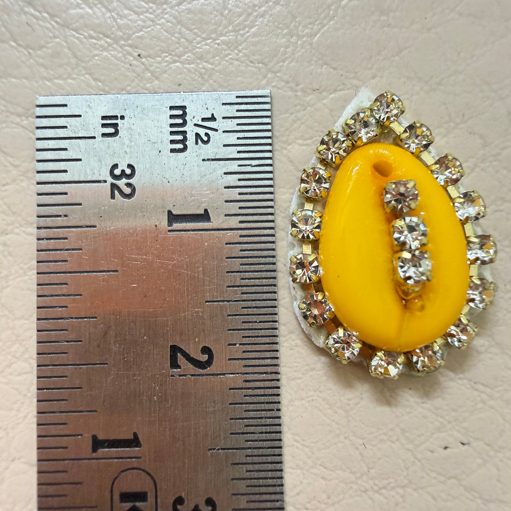 Yellow brooch with rhinestones next to a ruler for scale on a beige background