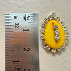 Yellow brooch with rhinestones next to a ruler for scale on a beige background