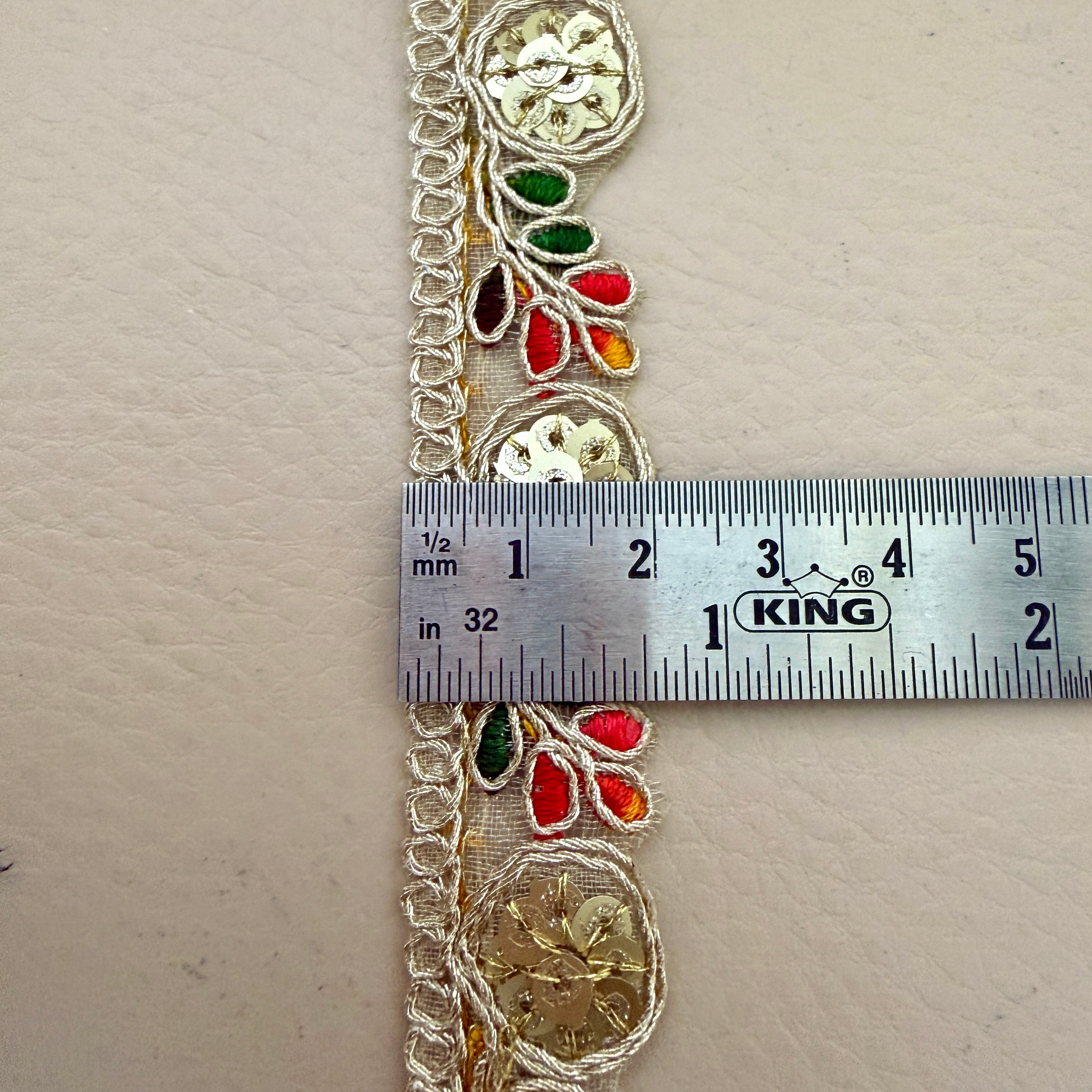 Decorative lace trim with colorful beads and a ruler for scale on a beige background