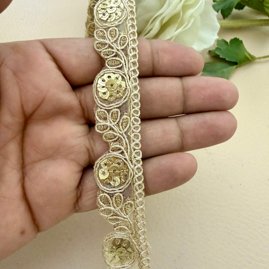 Gold lace trim held by a hand with a white flower in the background