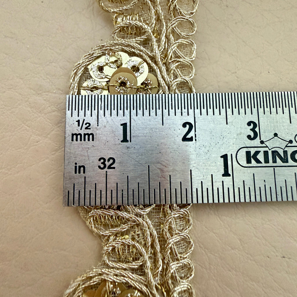 Decorative gold trim with sequins measured against a ruler on a beige background