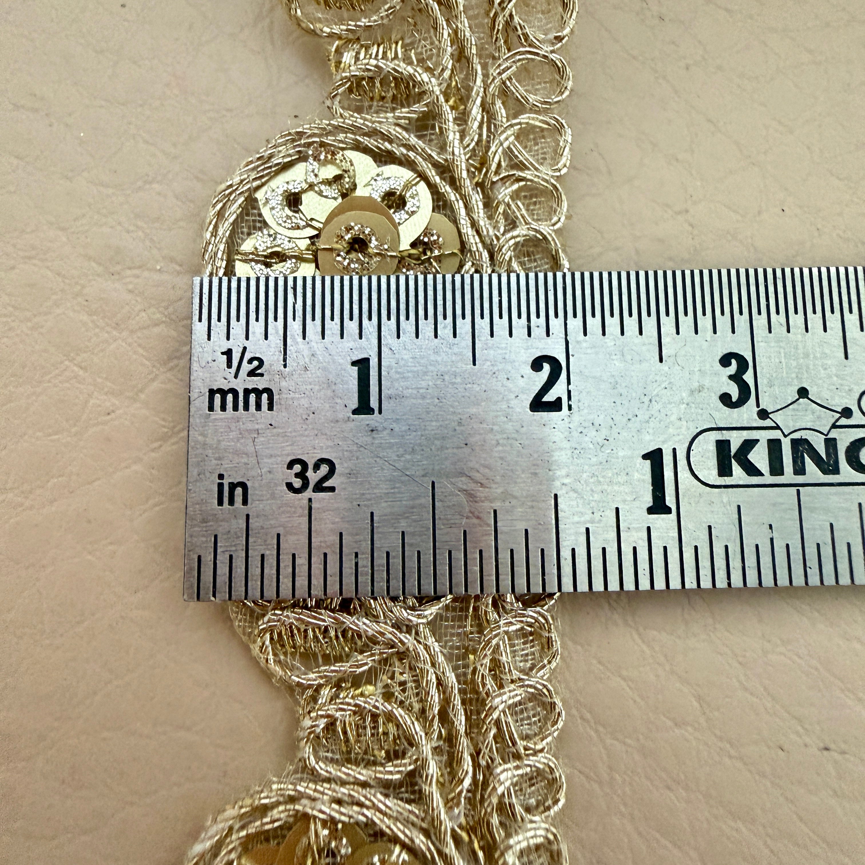 Decorative gold trim with sequins measured against a ruler on a beige background