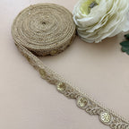Decorative lace ribbon with gold embellishments on a light surface next to a white flower.