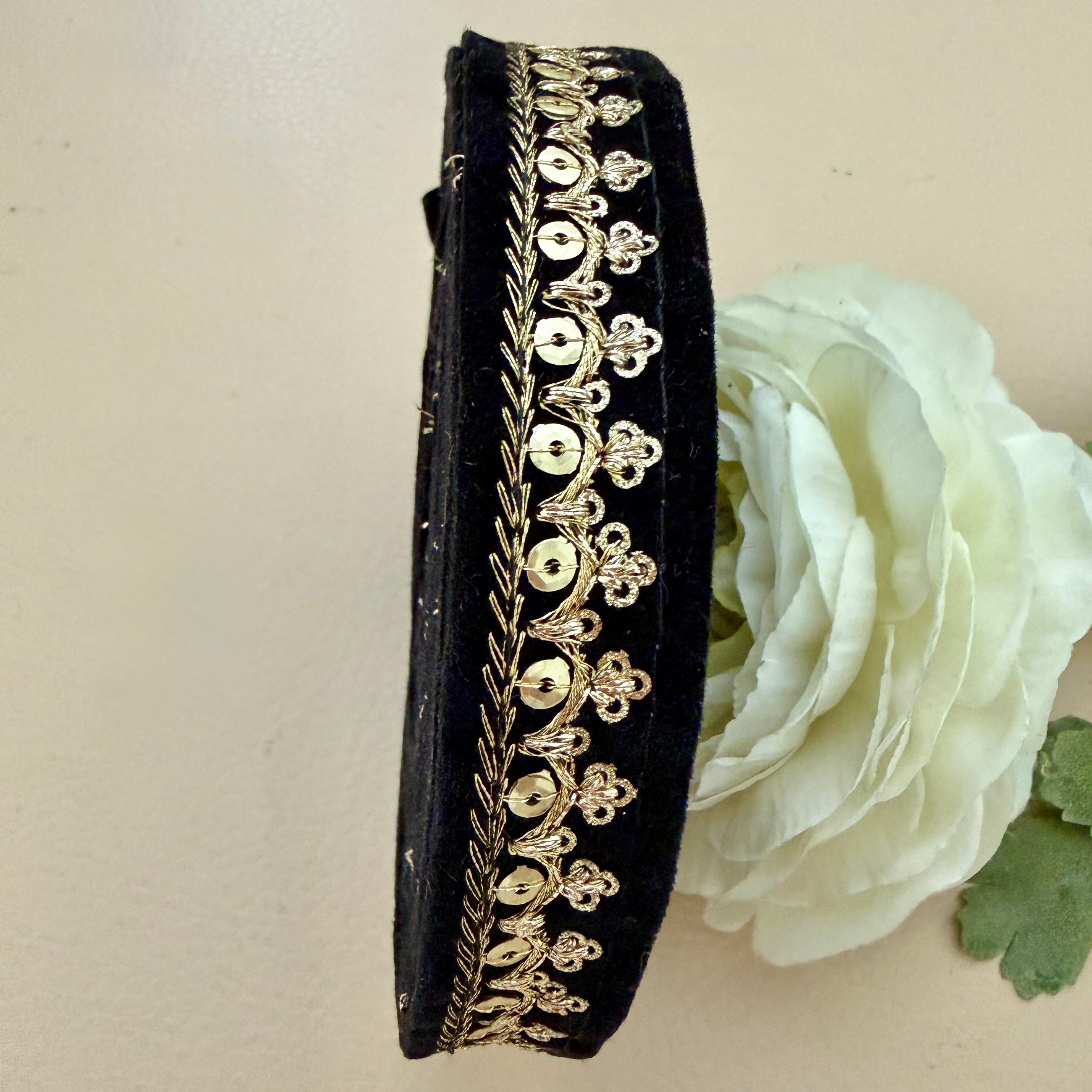 Black clutch with gold embroidery next to a white flower on a beige background
