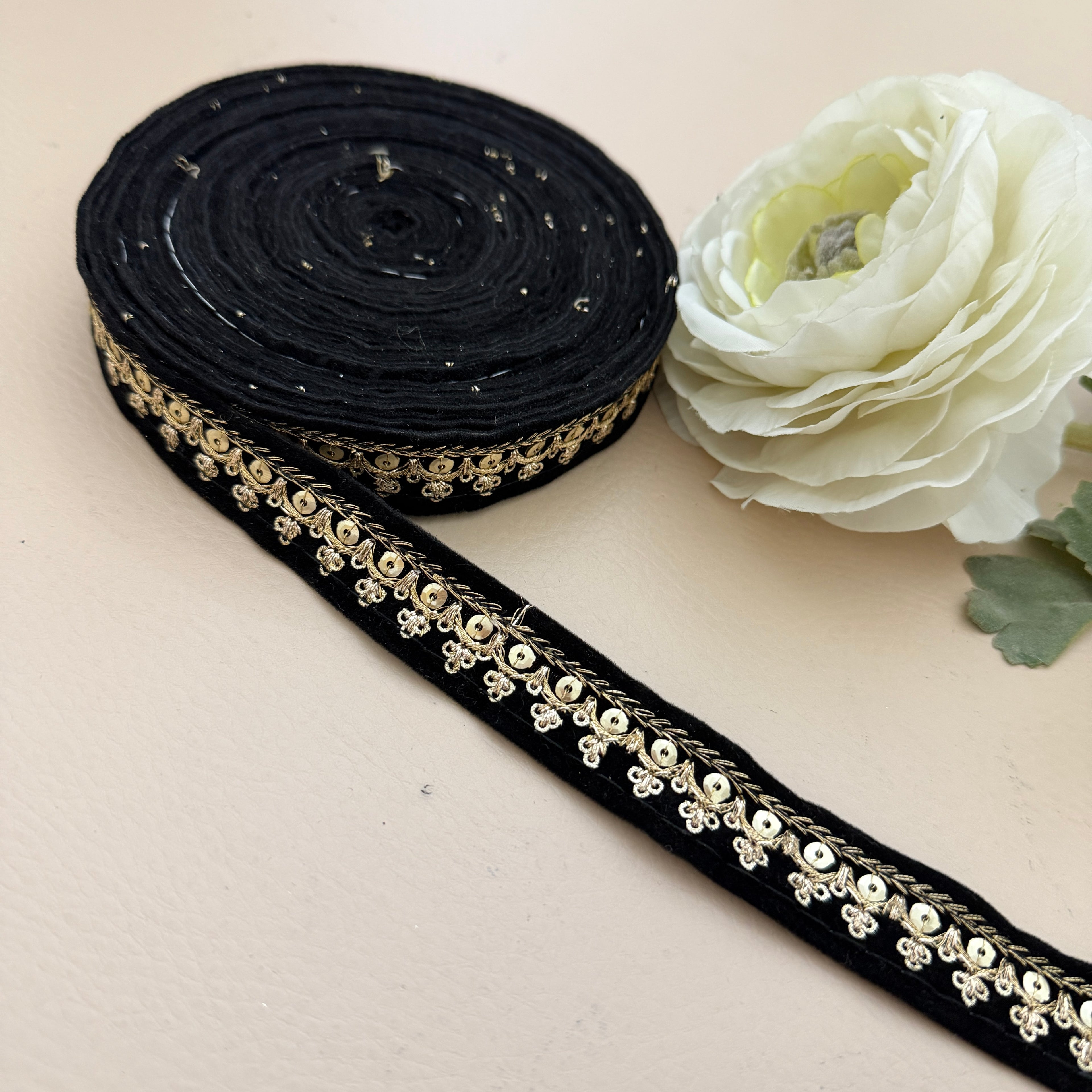 Black ribbon with gold embellishments next to a white flower on a beige background