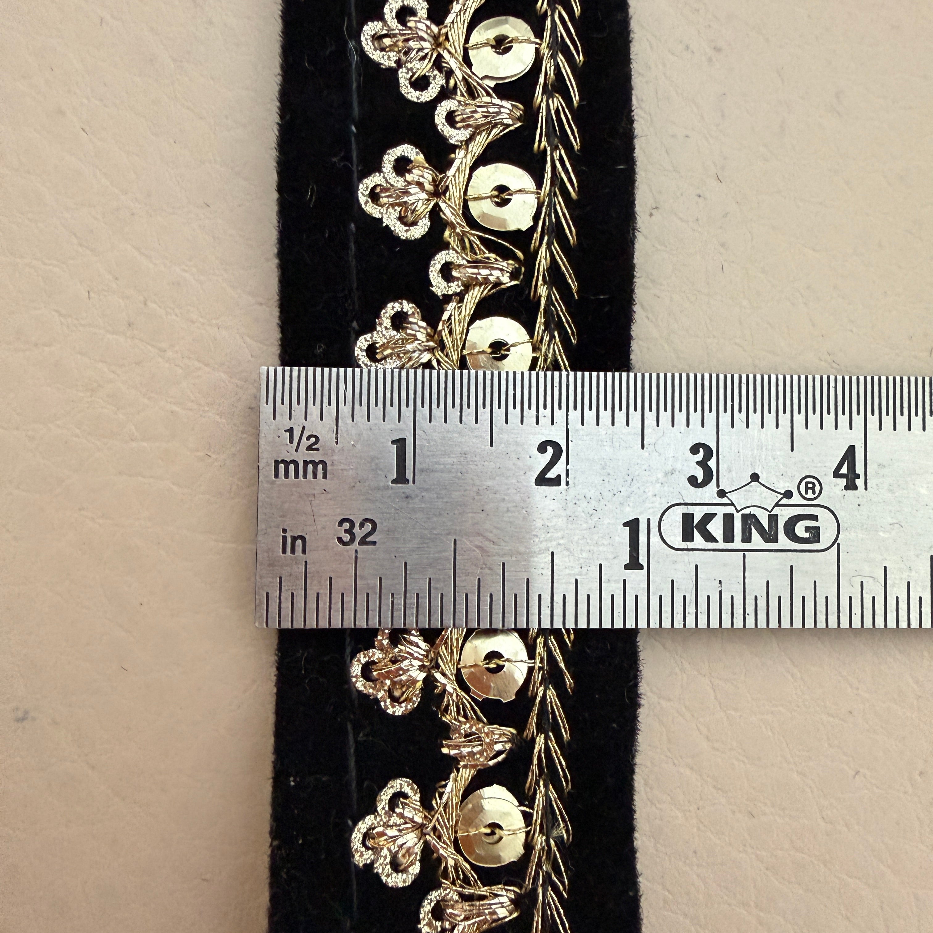 Gold floral embroidery on black fabric with a ruler for scale