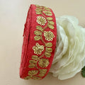 Red fabric ribbon with gold embroidery next to a white flower on a beige background