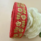 Red fabric ribbon with gold embroidery next to a white flower on a beige background