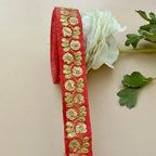 Red ribbon with gold floral embroidery on a beige background with a white flower and green leaves.