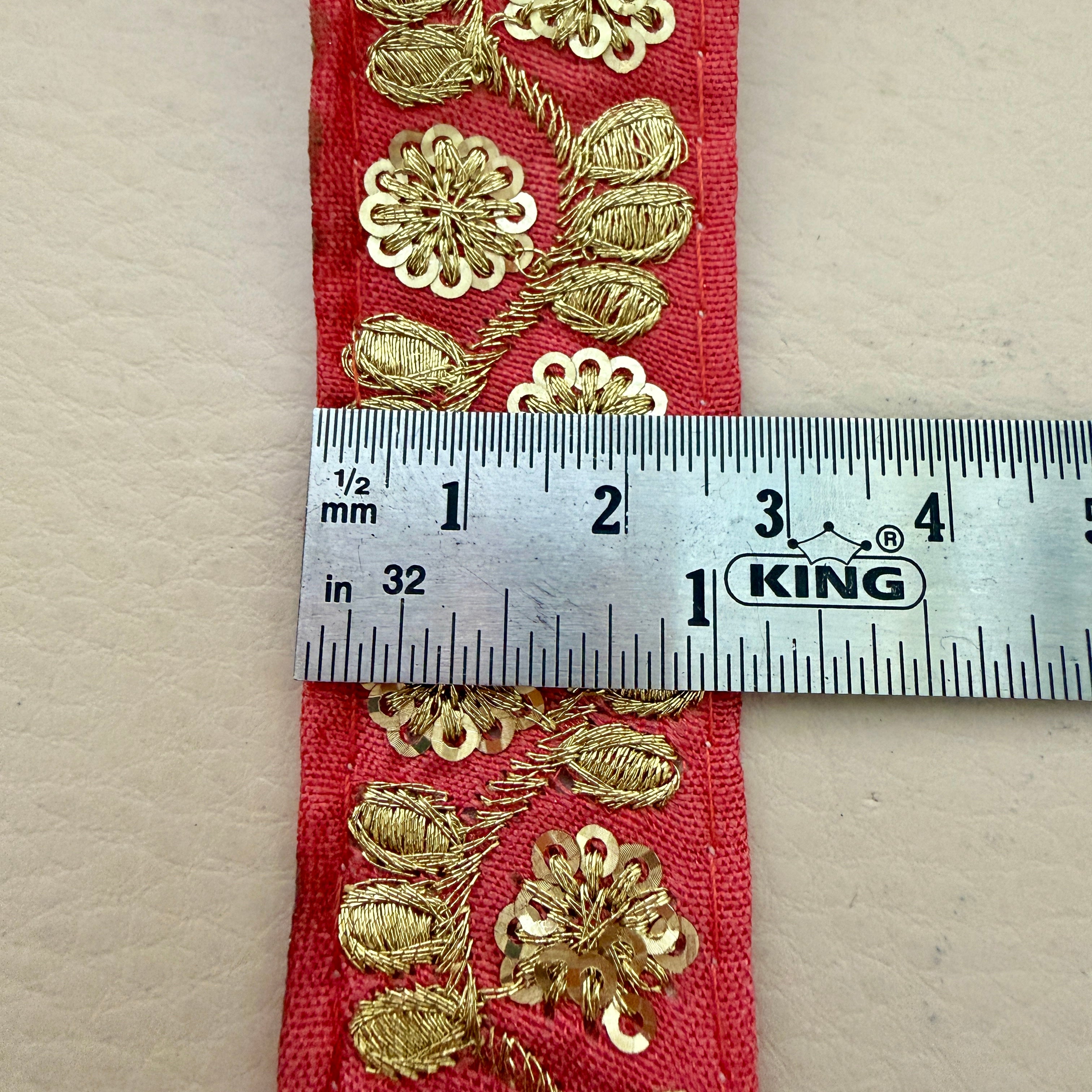 Red fabric with gold floral patterns and a ruler for measurement on a beige background