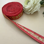 Roll of red fabric with gold embroidery next to a white flower on a beige background
