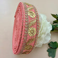 Roll of pink fabric with gold embroidery next to a white flower on a beige background