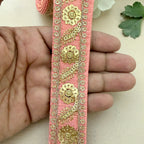 Decorative pink ribbon with gold floral embroidery held between fingers