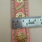 Decorative pink ribbon with gold floral patterns and a ruler for scale on a beige background