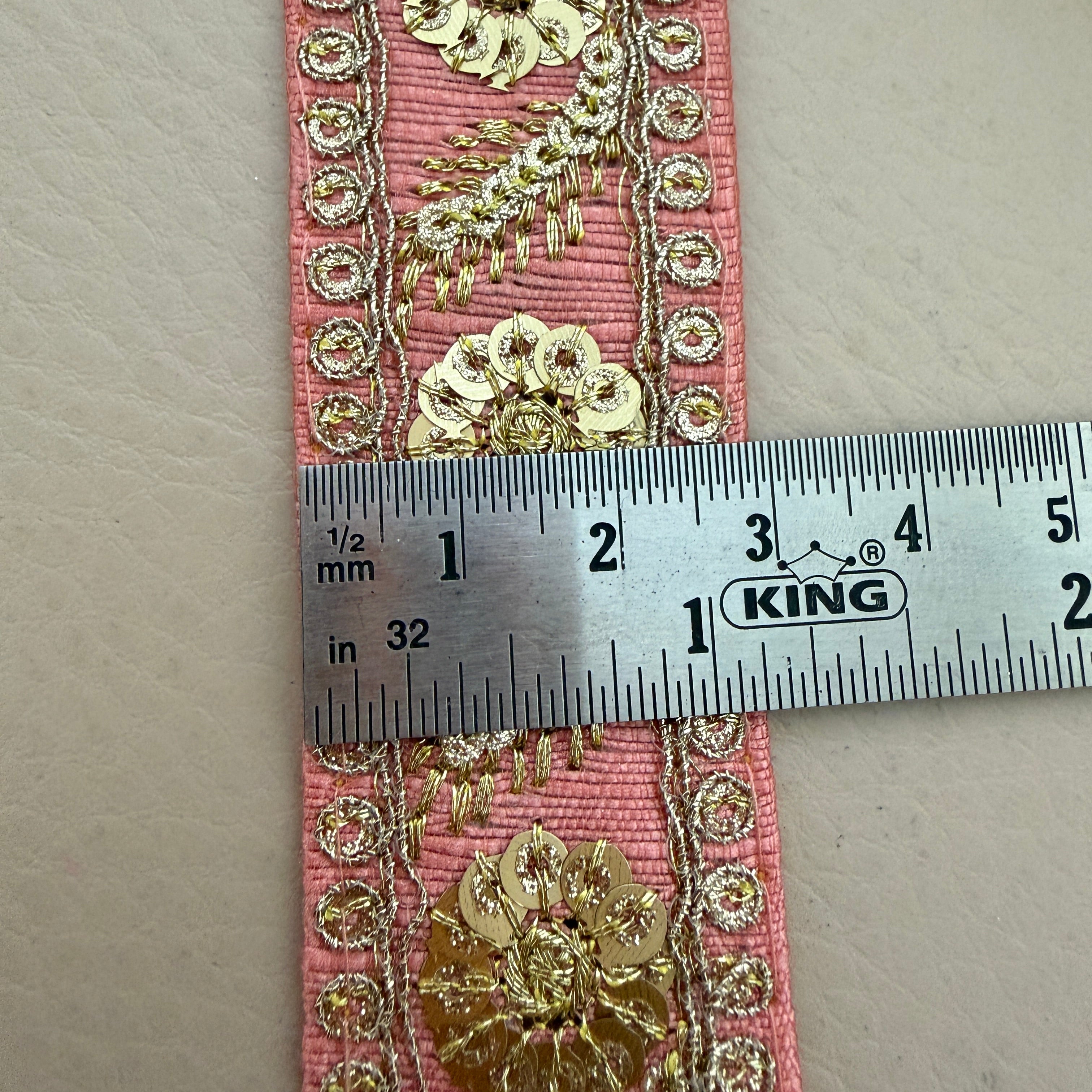 Decorative pink ribbon with gold floral patterns and a ruler for scale on a beige background