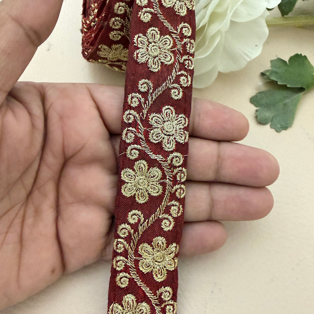 Red ribbon with gold floral embroidery held by a hand on a light background