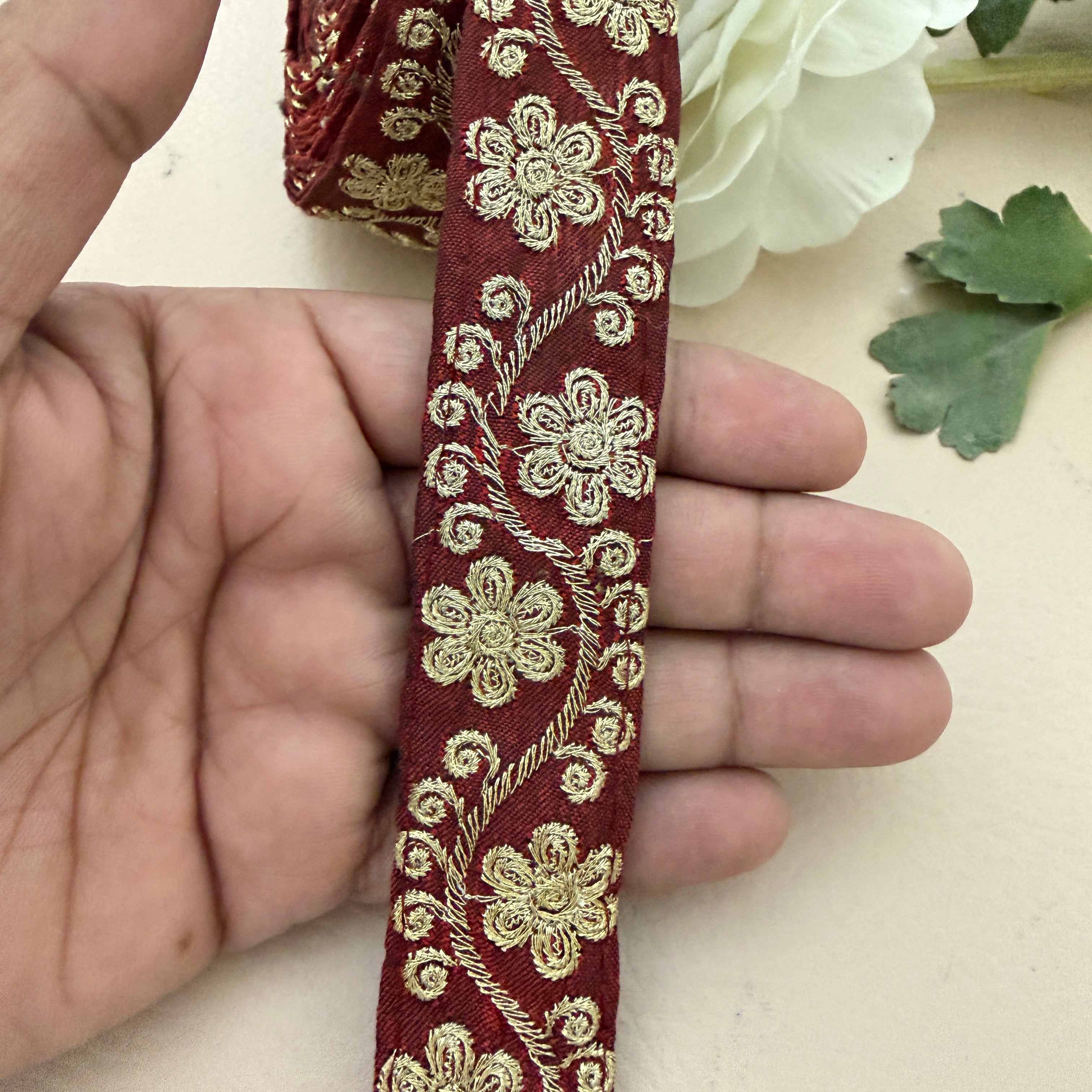 Red ribbon with gold floral embroidery held by a hand on a light background