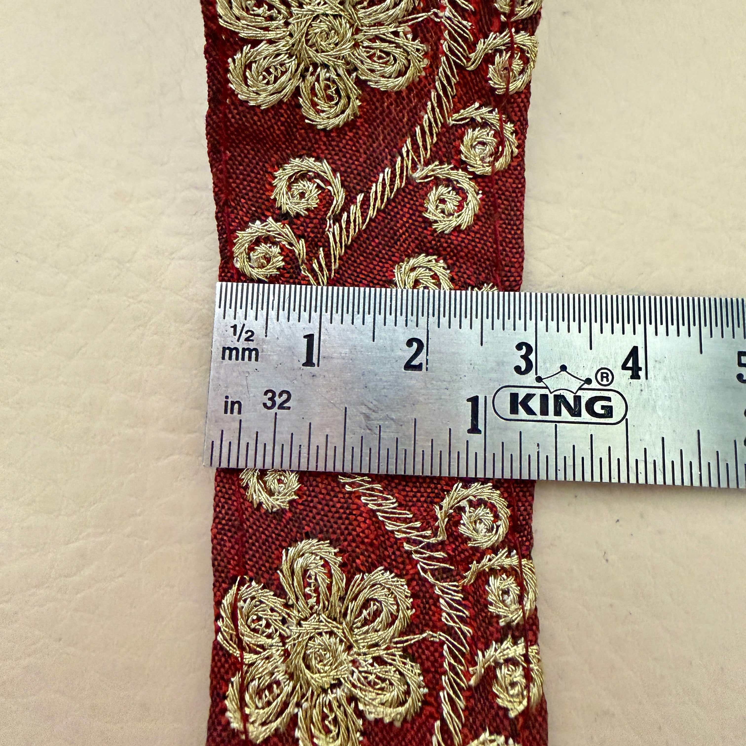 Red fabric with gold embroidery and a ruler for scale on a beige background