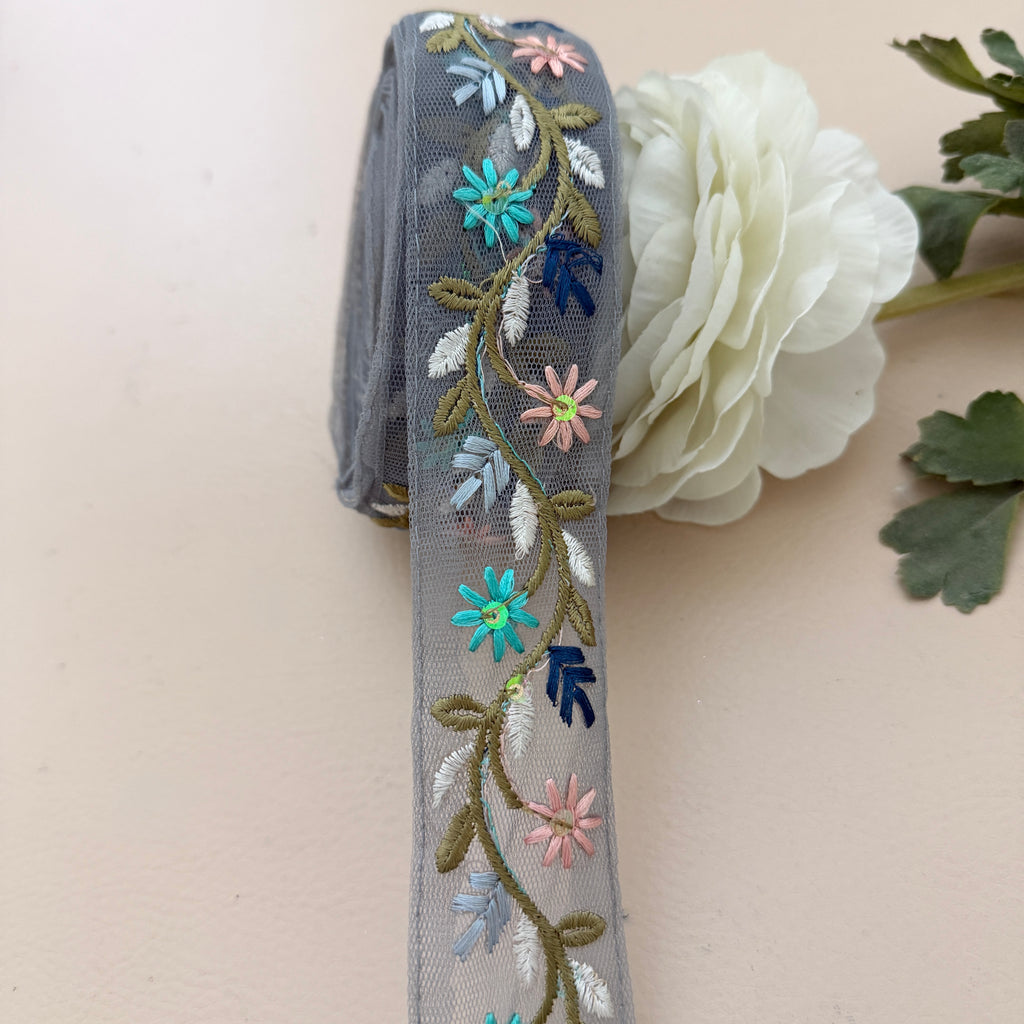 Embroidered ribbon with floral designs on a white flower and green leaves.