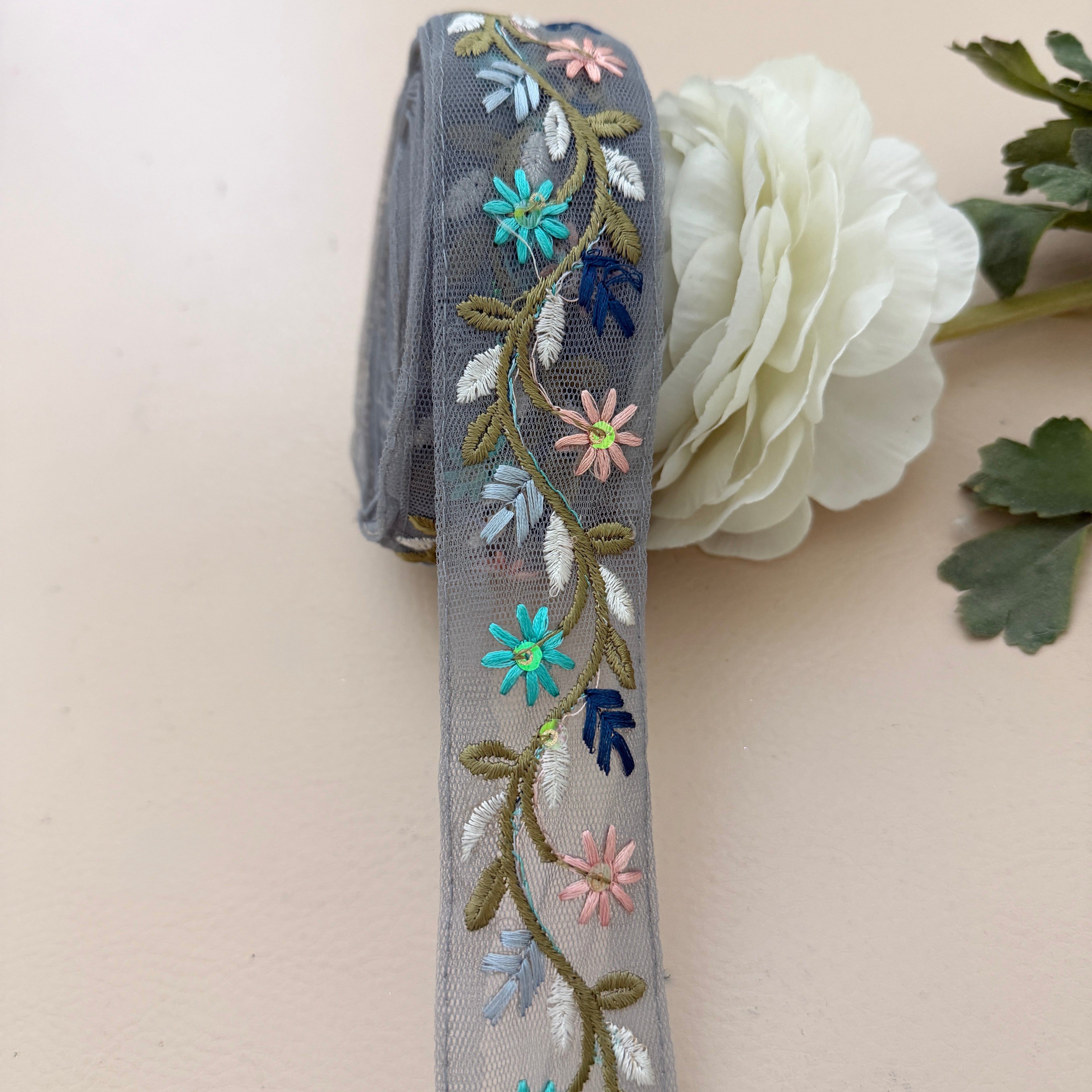 Embroidered ribbon with floral designs on a white flower and green leaves.