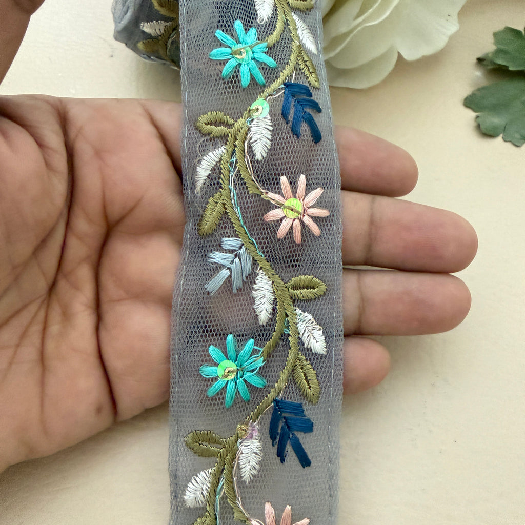 Embroidered floral ribbon held between fingers with a neutral background