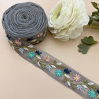 Embroidered ribbon with floral patterns next to a white flower on a beige background