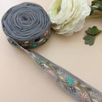 Embroidered ribbon with floral patterns on a beige surface next to a white flower.