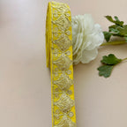 Yellow decorative ribbon with intricate patterns on a beige background with a white flower and green leaves.