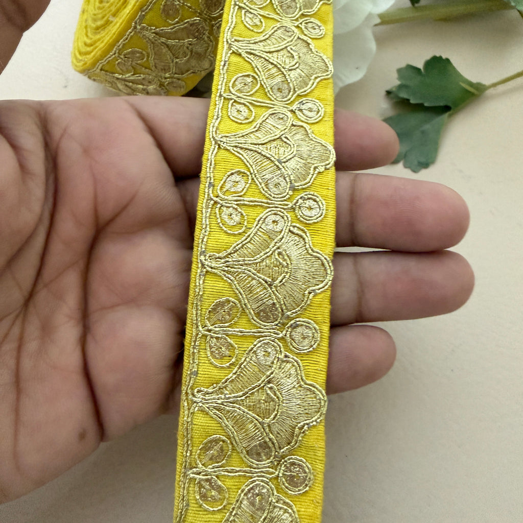 Yellow ribbon with intricate gold embroidery held between fingers on a light background