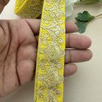 Yellow ribbon with intricate gold embroidery held between fingers on a light background
