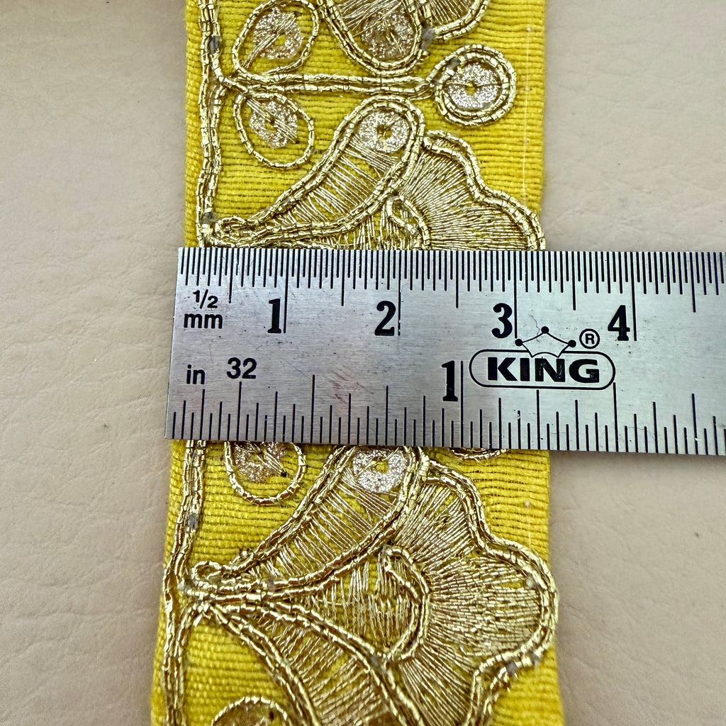 Yellow fabric with gold embroidery measurement against a ruler