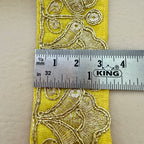 Yellow fabric with gold embroidery measurement against a ruler