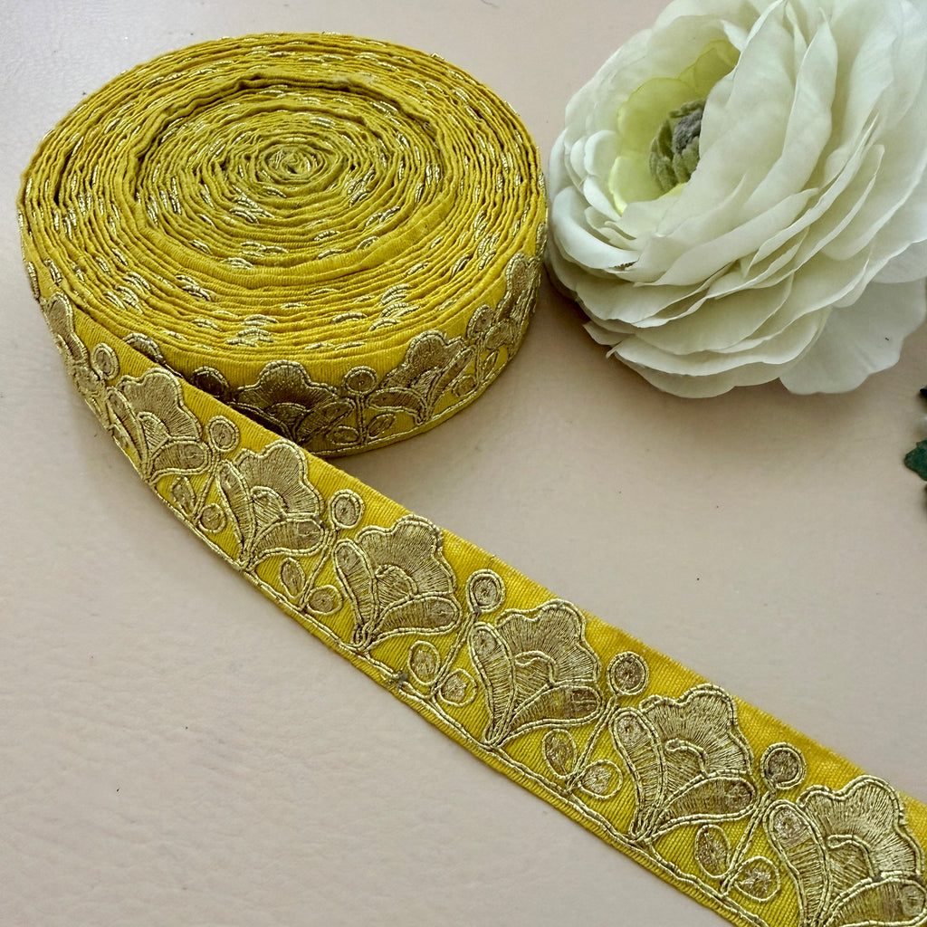 Roll of yellow lace ribbon with floral patterns next to a white flower on a light background